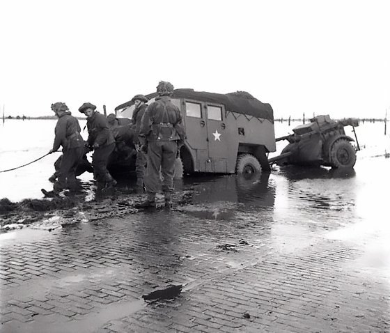 A military vehicle off the edge of a flooded road, with soldiers standing in the water